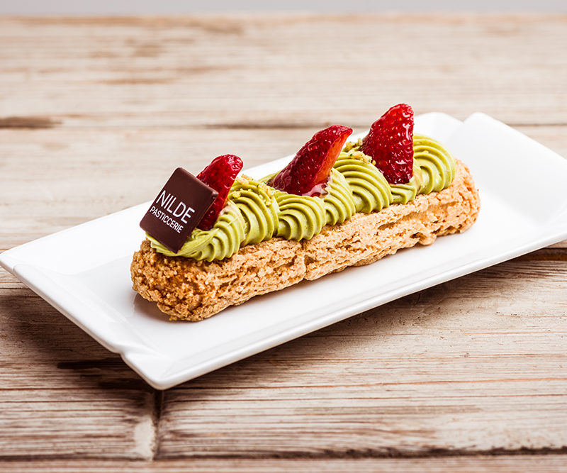 Praline eclair with pistachio and strawberry coulis